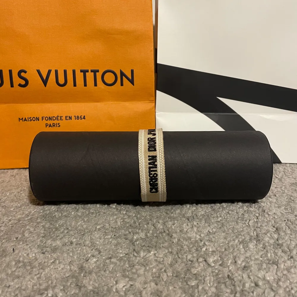 Snyggt beige armband från Christian Dior med texten 'Christian Dior J'adore' i svart. Armbandet har justerbara tofsar för en perfekt passform. Perfekt accessoar för att lyfta din stil.. Asusteet.