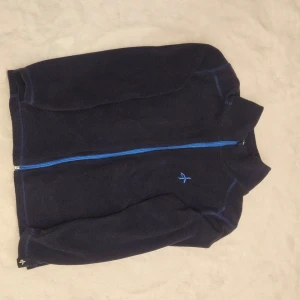 Mörkblå fleecejacka från Cross Sportswear - Säljer en mörkblå fleecejacka från Cross Sportswear med en dragkedja i ljusblått. Jackan har långa ärmar och är perfekt för kyligare dagar. Den är tillverkad i Sverige och har en stilren design.