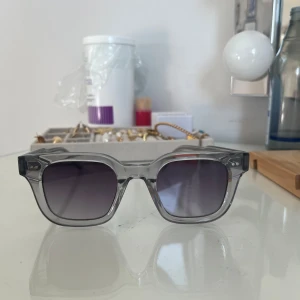 Grå solglasögon från Chimi - Snygga grå solglasögon från Chimi med transparent båge och mörka linser. Perfekta för en stilren look. Kommer med ett vitt fodral och putsduk. Modell 04 och knappt använda.