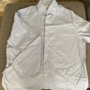 Ljusblå skjorta från These Glory Days - Säljer en stilren ljusblå skjorta från These Glory Days. Skjortan har en klassisk krage och knappar framtill. Den är långärmad och har en normal passform, perfekt för en avslappnad men ändå uppklädd look.