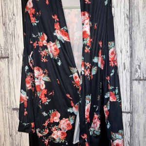 Svart blommig kimono - Snygg svart kimono med ett färgglatt blommönster i rött och grönt. Den har långa ärmar och ett luftigt, öppet snitt som ger en avslappnad känsla. Perfekt för att lägga till en touch av stil till din outfit.