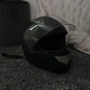 Mopedhjälm viarelli - Mopedhjälm från Viarelli med klart visir. Hjälmen har en aerodynamisk design och ventilationsöppningar, godkänd E9. Aldrig  avramlad med men har några skrapsår från mopedens sits när man stänger. Sparsamt använd.  Storlek m /56-58 Nypris 1299kr