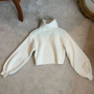 Vit stickad polotröja - Säljer en mysig vit stickad polotröja med ribbad design. Tröjan har långa ärmar och en hög polokrage som håller dig varm. Perfekt för kyliga dagar!