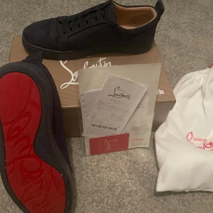   Christian Louboutins - Mörk blåa sneakers från Christian Louboutin med den ikoniska röda sulan. Skorna har snörning och är tillverkade i ett elegant material med broderad logga på hälen. Perfekta för den som vill sticka ut denna sommar. Priset är ej hugget i sten. Hör av dig för mer info