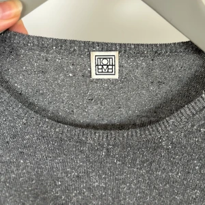 Grå stickad t-shirt från Totême - Säljer en stilren grå stickad t-shirt från Totême. Den har en melerad look med korta ärmar och rund hals. Perfekt för en avslappnad men ändå snygg stil. Passar bra till både jeans och kjol. 🖤