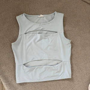 Ljusblå ärmlös topp - Säljer en stilren ljusblå ärmlös topp med unika utskärningar framtill. Perfekt för en trendig look. Passar bra till både jeans och kjol.