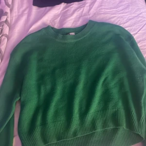 Grön stickad tröja - Säljer en snygg grön stickad tröja med rund halsringning. Perfekt för kyligare dagar och ger en skön och avslappnad look. Tröjan har långa ärmar och ribbade kanter för extra komfort.