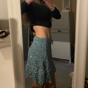 Blommig kortkjol i blått och grön - Söt kortkjol med blommigt mönster i grönt och vitt. Den är gjord i ett mjukt och bekvämt material som ger en skön passform. Perfekt till sommaren!