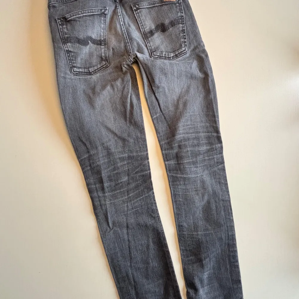 Snygga grå jeans från Nudie Jeans med en klassisk straight passform. De har en stilren design med fickor och knappgylf. Perfekta för en avslappnad look. Jeansen har lite nött mellan benen men inga håll. Skriv privat om du har några funderingar💕. Farkut & Housut.