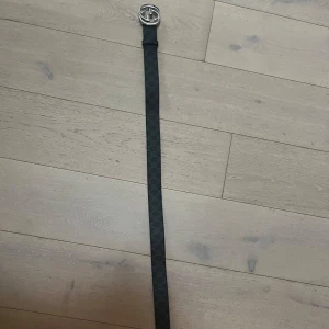 110 cm Svart bälte med mönster och silverdetaljer - Snyggt svart bälte med diskret mönster och en stilren silverfärgad spänne. Baksidan är brun vilket ger en fin kontrast. Perfekt för att lyfta vilken outfit som helst.