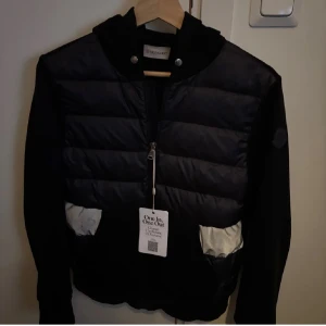 Moncler cardigan  - Säljer en snygg svart cardigan jacka från Moncler med dragkedja och huva. Jackan har långa ärmar och en stilren design med vita detaljer vid fickorna. Perfekt för kyligare dagar. Kvitto och äkthetsbevis finns 