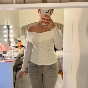 Vit offshoulder topp - Säljer en stilren vit offshoulder topp med långa ärmar. Perfekt för en elegant look. Toppen har en tight passform som framhäver figuren.