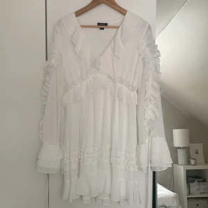 Vit klänning från Boohoo - Säljer en vit klänning från Boohoo med volanger och långa ärmar. Klänningen har en romantisk stil med flera lager av volanger och en lös passform. Perfekt för en somrig look!