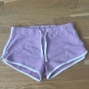 Ljuslila shorts från FASister - Säljer ett par ljuslila shorts från FSister i mjuk bomull. De har vit kant runtom och snörning i midjan för perfekt passform. Perfekta för sommardagar eller chill hemma. Klassisk sportig look med loose fit. Storleken är fel då den sitter lite thight på mig som är strl S så jag skulle rekommendera att köpa dom ifall du är storlek Xs.