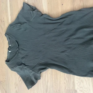 Ribbad grön T-shirt  från Lindex - Superskön ribbad t shirt från Lindex i en mörkgrön nyans. Klänningen har korta ärmar och en enkel, avslappnad passform. Perfekt för dig som gillar en stilren och bekväm look.