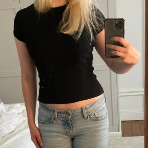 Svart ribbad topp från Weekday - En svart, ribbad topp från Weekday med korta ärmar och rund hals. Modellen är tight och croppad, perfekt att styla med jeans eller kjol. Enkel och stilren design som funkar till många olika looks.