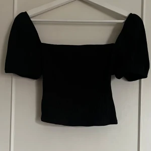 Svart offshoulder topp med puffärm - Trendig svart topp med offshoulder-design och puffiga korta ärmar. Croppad modell i ribbat material som ger en snygg struktur.