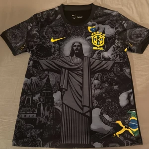 Brasil Nike fotbollströja svart/gul - Unik Brasilien fotbollströja från Nike med svart och grått konstnärligt tryck av Kristusstatyn och brasilianska symboler. Gula detaljer, broderat CBF-märke och flagga på ärmen. Tillverkad i lätt, ventilerande material. Perfekt för dig som vill sticka ut på planen eller läktaren.
