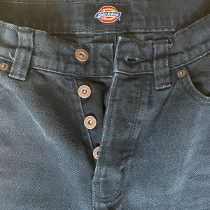 Svarta jeans från dickies! - Svarta jeans från dickies!! De är högmidjade och har en rak passform, knappar som gylf och i storlek w26⭐️ använda men inte slitna, finns inga hål eller skav på. Jag brukar ha s-m i byxor och är 165, de går precis ner till anklarna på mig💕 