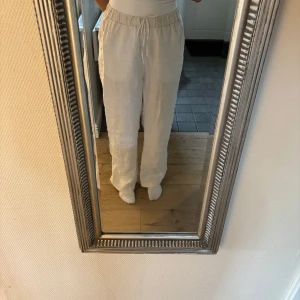 Vita linnebyxor med snörning - Säljer ett par vita linnebyxor med avslappnad passform och breda ben. Byxorna har resår i midjan och snörning för extra komfort. Perfekta för varma dagar och chill vibes.
