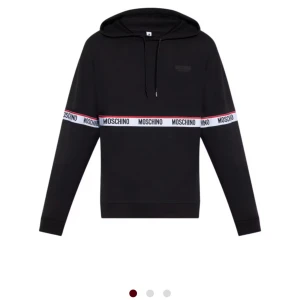 Svart hoodie från Moschino med logoband - Svart hoodie från Moschino med huva och snörning. Tröjan har ett vitt logoband med röd kant och Moschino-tryck som går runt bröstet och armarna. Säljs pga att jag inte känner att jag vill ha mycket märkes kläder längre storlek S men passar M om du vill ha en lite tightare huvtröja.Haft tröjan nått år men bara använt vid finare tillfällen. Kvittot är borttappat eller slängt men tröjan är självklart äkta. Hör av er vid intresse! Mvh