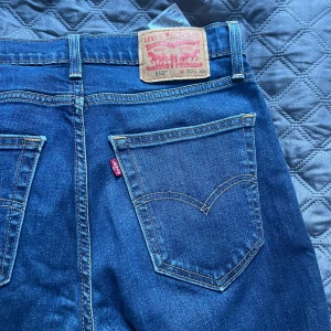 Levi's 512 blå jeans W30 L30 - Säljer ett par klassiska Levi's 512 jeans i blå denim. Modellen har smal passform med raka ben och snygga kontrastsömmar. Ikonisk läderpatch bak och röda Levi's-tag på fickan. Perfekta jeans för dig som gillar en tidlös look.