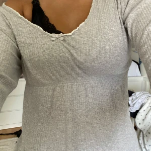 Grå ribbad topp från Odd Molly - Supersöt ljusgrå ribbad topp från Odd Molly med lång ärm, v-ringning och liten rosett framtill. Fina spetsdetaljer vid halsringningen. Använd ett fåtal gånger❤️