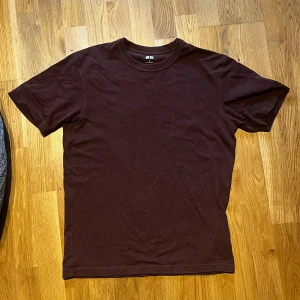 Mörkbrun t-shirt från Uniqlo - En basic mörkbrun t-shirt från Uniqlo i klassisk modell. T-shirten har rund halsringning och korta ärmar, tillverkad i mjuk bomull. Perfekt för en clean och enkel stil.