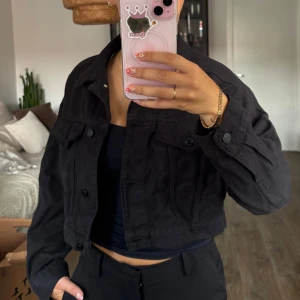 Svart croppad jeansjacka Gina Tricot - Svart croppad jeansjacka från Gina Tricot med klassisk krage, knappar framtill och två bröstfickor. Jackan har en loose passform. 