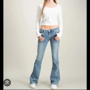 Ljusblå bootcut jeans med fickdetaljer - Säljer ett par ljusblå bootcut jeans från True Religion med snygga bakfickor med lock och knapp. Jeansen har låg midja, klassisk femficksdesign och är tillverkade i stretchig denim för en bekväm passform. Perfekta för dig som gillar retrovibbar och coola detaljer.