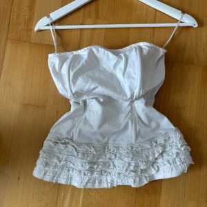 Vit korsettopp med volang  - Supersöt vit korsettopp från Topshop i storlek M. Toppen har lite fläckar som troligen går bort i tvätten. Se alla bilder!💕