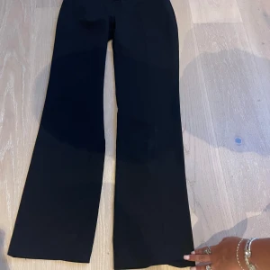 Svarta extra lowwaist, bootcut kostymbyxor - Säljer ett par svarta kostymbyxor med bootcut-silhuett. Byxorna har en extra lågmidja och vida ben som ger en snygg och trendig look. Perfekta att styla med sneakers eller klackar för en clean vibe.