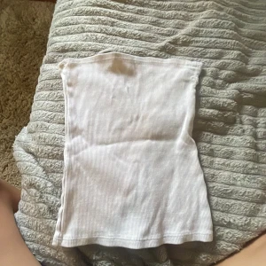 Vit ribbad tubtopp från H&M XS - En enkel och stilren vit tubtopp från H&M i storlek XS. Toppen är ribbad och har bandeau-modell, perfekt för att matcha med jeans eller kjol. Mjuk och stretchig känsla som sitter snyggt på kroppen.