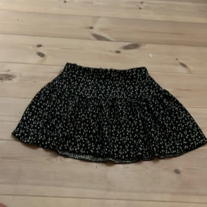 Svart blommig kortkjol Gina Tricot - Supersöt svart kortkjol från Gina Tricot med små vita blommor över hela tyget. Kjolen har en volangig och luftig form som ger en skön vibe. Perfekt att matcha med en enkel topp eller hoodie för en chill look.