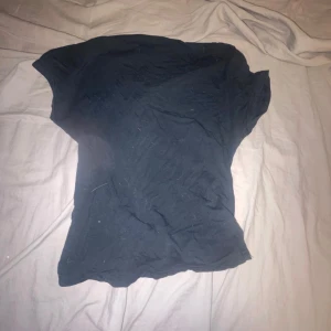 Svart croppad topp med öppen rygg - En svart croppad topp i stretchigt material med korta ärmar och öppen rygg. Snygg och enkel design som sitter tight och framhäver midjan. Perfekt för dig som gillar minimalistisk stil med en twist på ryggen.