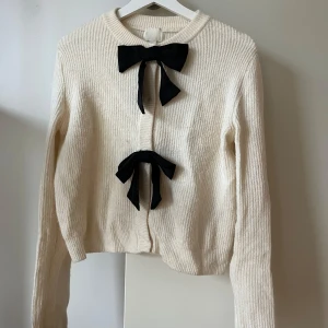 Vit kofta med svarta rosetter H&M - Superfin vit ribbstickad kofta med två stora svarta rosetter framtill, långärmad och mjuk 🤍Storlek M från H&M