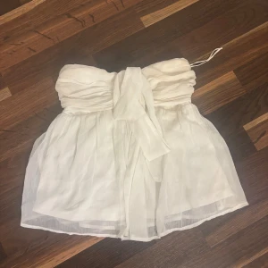 Vit bandeau tubtopp från Nelly - Supersöt vit bandeau tubtopp från Nelly med voluminös, transparent look och bred knytrosett framtill. Toppen har smockad rygg för extra komfort och sitter snyggt axelbandslöst. Perfekt för sommarens alla tillfällen!