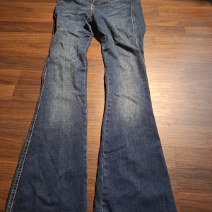 Blå bootcut jeans från Dr Denim - Säljer ett par klassiska blå jeans från Dr Denim med bootcut-ben och snygga kontrastsömmar. Jeansen har normal midja, fem fickor och är tillverkade i slitstarkt denimtyg. Perfekta för dig som gillar retrovibbar och vill ha en tidlös look. De är I storlek S i midjan och 32 i längden
