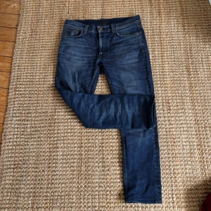 Mörkblå jeans från Nudie Jeans - Storlek 30/30 dem är skit snygga men har tyvärr blivit lite för lång för dem Snygga mörkblå jeans från Nudie Jeans med klassisk femficksdesign och ikoniska vågdetaljer på bakfickorna. Jeansen har en rak passform och är tillverkade i slitstarkt denimtyg. Perfekta för dig som gillar en tidlös och clean look.