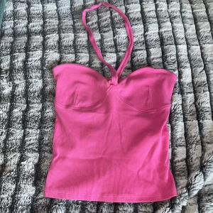Rosa halterneck topp från Gina Tricot - Säljer en snygg rosa halterneck topp från Gina Tricot i ribbat material. Toppen har en croppad passform och markerade kupor för en cool siluett. Perfekt för dig som vill sticka ut med färg och stil i sommar!