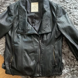 Svart skinnjacka från Esprit - Snygg svart skinnjacka från Esprit med coola dragkedjor och quiltade detaljer baktill. Jackan har en klassisk krage och raka linjer som ger en stilren vibe. Perfekt för dig som vill ha en tidlös och edgy look.