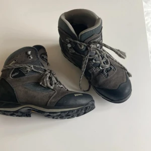 Grå vandringskängor från Meindl Gore-Tex - Stabila grå vandringskängor från Meindl med Gore-Tex-membran. Ovandel i mocka och slitstark textil, robust snörning och grov Vibram-sula för extra grepp. Perfekta för hiking och äventyr utomhus.
