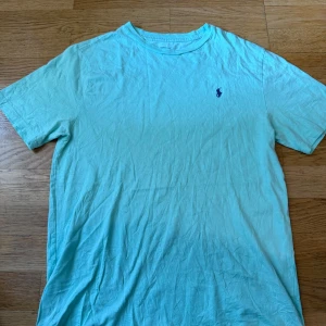 Turkos t-shirt från Polo Ralph Lauren - Snygg turkos t-shirt från Polo Ralph Lauren med klassisk broderad logga på bröstet. T-shirten är i mjuk bomull och har en avslappnad passform med korta ärmar. Perfekt för dig som gillar stilrena och bekväma plagg.