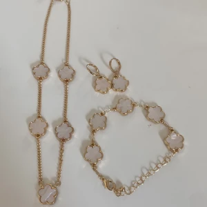 Guldpläterat smyckeset med blommor - Snyggt smyckeset med halsband, armband och örhängen i guldpläterad metall. Alla delar har vita blommor i pärlemor-look, infattade i guldram. Kedjorna är tunna och eleganta, och blommorna har en mjuk, rundad form som ger en lyxig känsla.