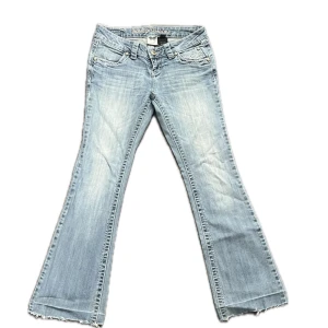 Lågmidjade Bootcut jeans Harley-Davidson ljusblå - Så sjukt snygga lågmidjade bootcut jeans från Harley Davidson med jättefina strass detaljer på fickorna! Står storlek 4, skulle säga att det är storlek 34 eller 36 i svenska mått. Midjemått 37 cm, innerbenslängd 72 cm 