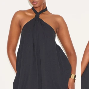  Söker!!! Svart halterneckklänning - Stilren svart klänning med halterneck och lös passform. Klänningen har en snygg knut vid halsen och faller mjukt över kroppen. Perfekt för dig som gillar minimalistisk och trendig stil.