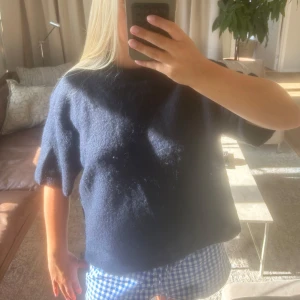 Mörkblå stickad tröja med kort ärm - Mysig mörkblå stickad tröja med korta ärmar och rund hals. Tröjan har en loose passform och är perfekt för lager-på-lager. Enkel och stilren design som funkar till många olika outfits. Tröjan är i L o jag har vanligtvist S/M. 