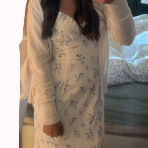 Vit långklänning med blå blommor - Superfin långklänning i vit med blått blommönster och smala axelband. Klänningen har en feminin v-ringning och en snygg slits på sidan. Perfekt för sommarens alla tillfällen, med en lätt och luftig känsla. Klänningen har endast används en gång för skolavslutningen och har varit orörd sen dess! 🙌Priset går att diskuteras💕