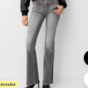 Grå bootcut jeans med hög midja - Snygga grå jeans med bootcut och mid Waist. Byxorna har markerade sömmar framtill och klassisk femficksdesign. Jeansen har en lätt tvättad look och stängs med dubbla knappar och dragkedja.