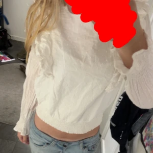 Vit blus med volang och struktur - Säljer en supersöt vit blus med volangdetaljer längs framsidan och ärmarna. Säljer då den är för kort i armarna på mig men har aldrig använt💗
